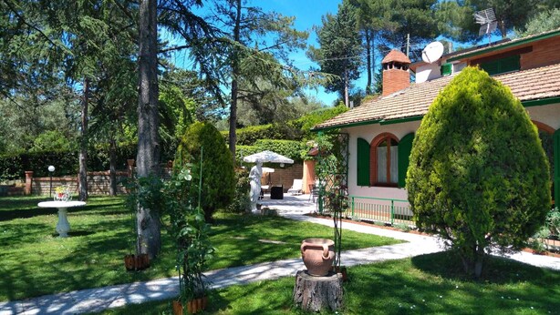 A well-maintained garden with a patio, a statue, and a rustic building with a tiled roof.