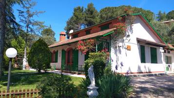 Un edificio tradicional con techo de tejas, contraventanas verdes y una estatua en el jardín.