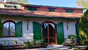 A two-story building with a tiled roof, green shutters, and a white facade.