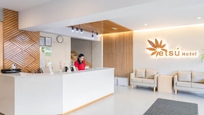 A modern hotel reception area with a reception desk, a receptionist, and a seating area with two sofas. - Etsu Hotel (Tacloban)