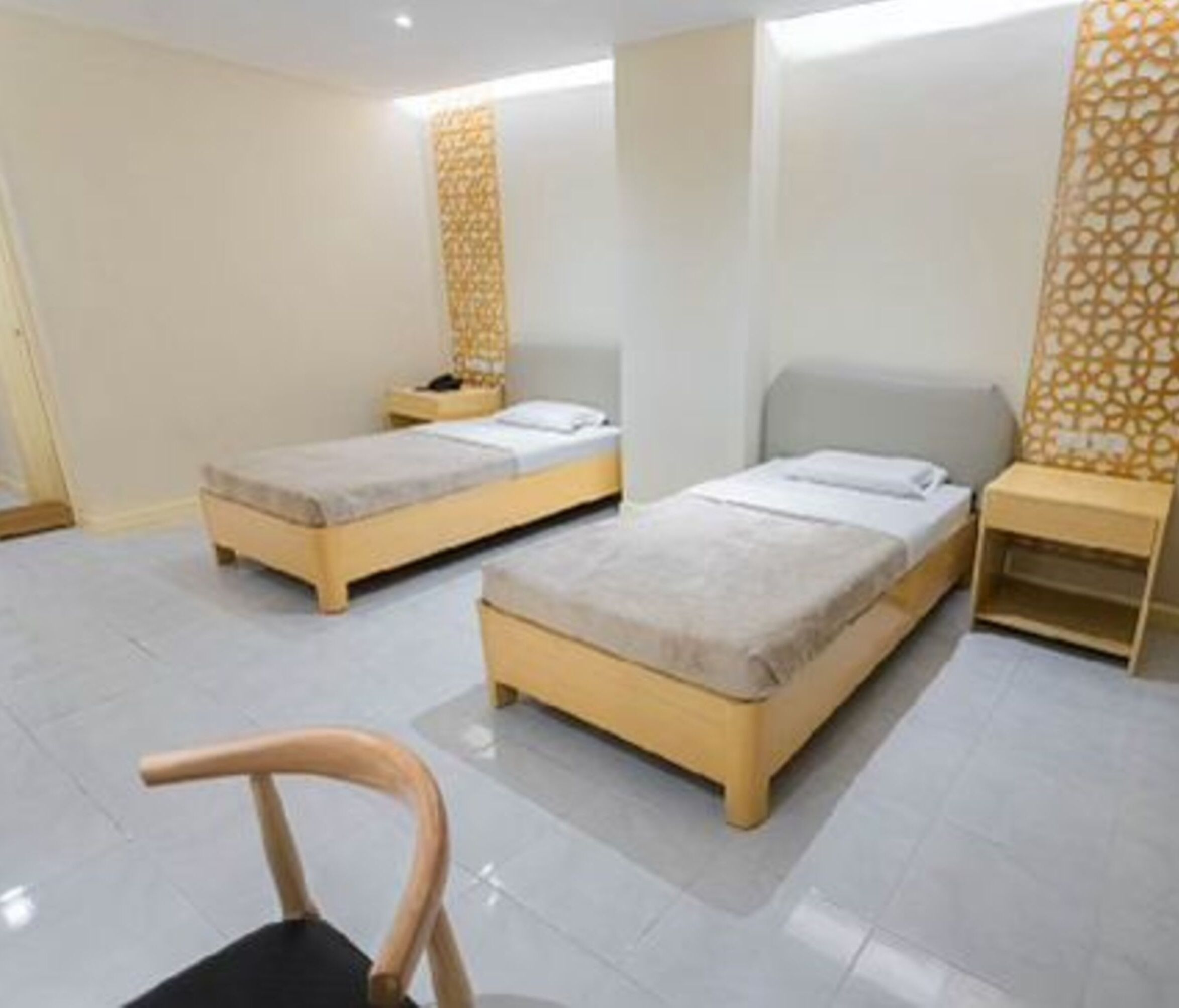 Une chambre d’hôtel avec deux lits simples, une chaise en bois, une table de chevet et un panneau décoratif mural.