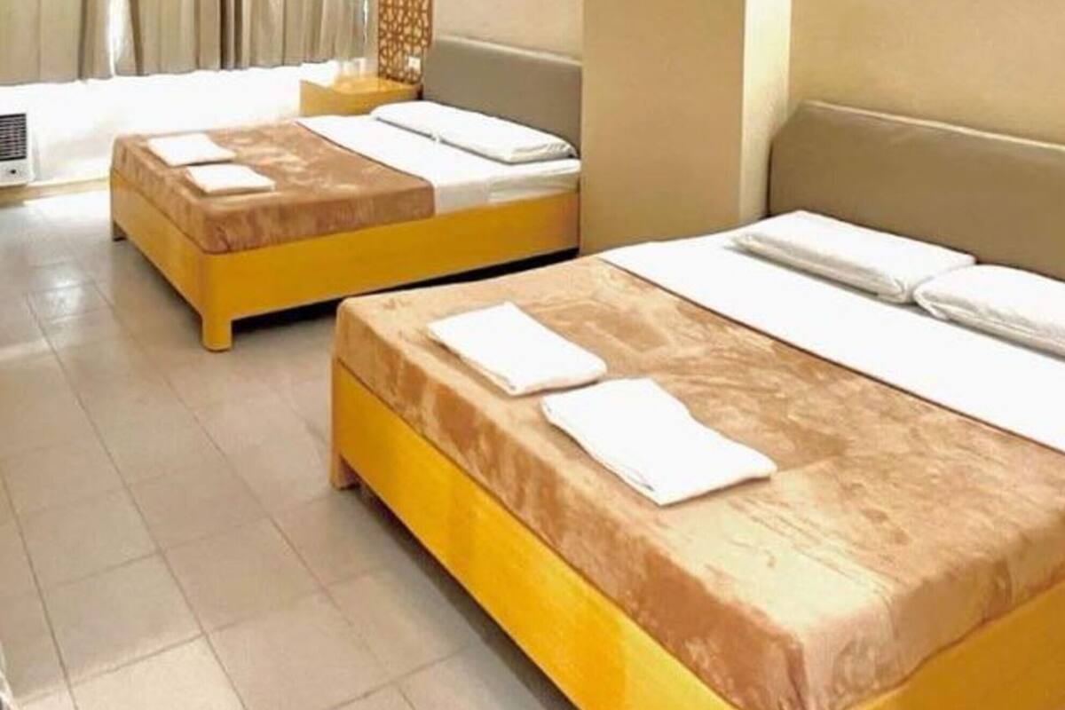 Ein Hotelzimmer mit zwei Betten, jeweils mit einer gelb-braunen Tagesdecke und weißen Bettwäsche.