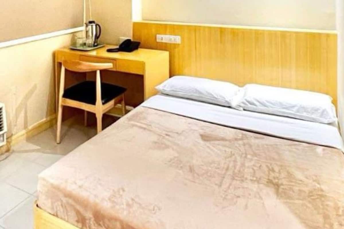 Ein Hotelzimmer mit einem Bett, einem Holztisch mit Stuhl, einem Telefon und einer Wandleuchte.