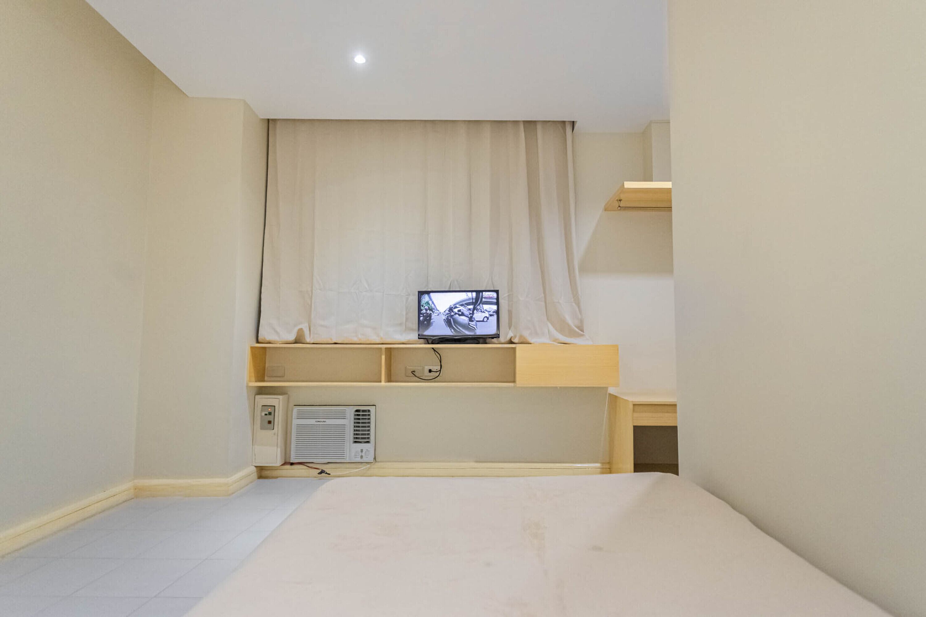 A bedroom with a bed, a television on a shelf, and a heater.