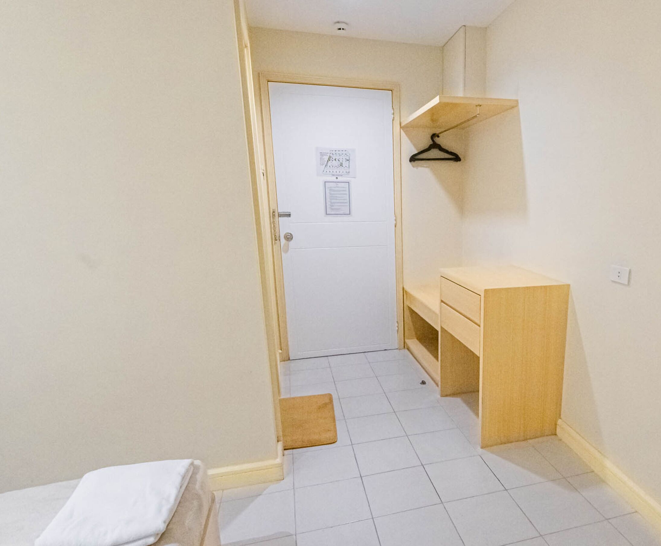 A small, clean room with a wooden desk, a white door, and a small shelf.