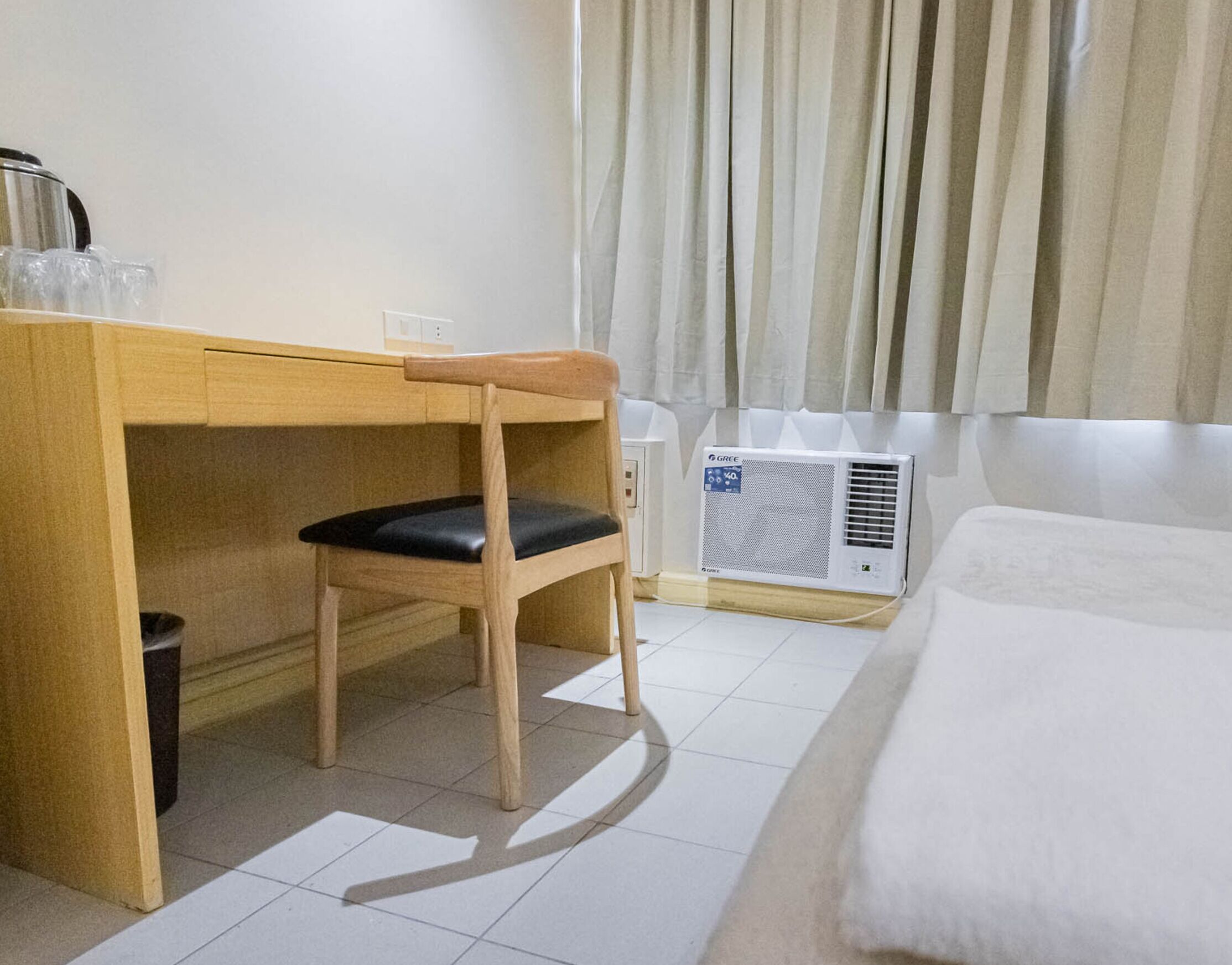 A hotel room with a wooden desk, a chair, a bed, and a window with curtains.