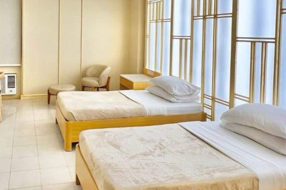 Ein Hotelzimmer mit zwei Holzbetten, einem kleinen Tisch, einem Stuhl und einem Fenster mit Jalousien.
