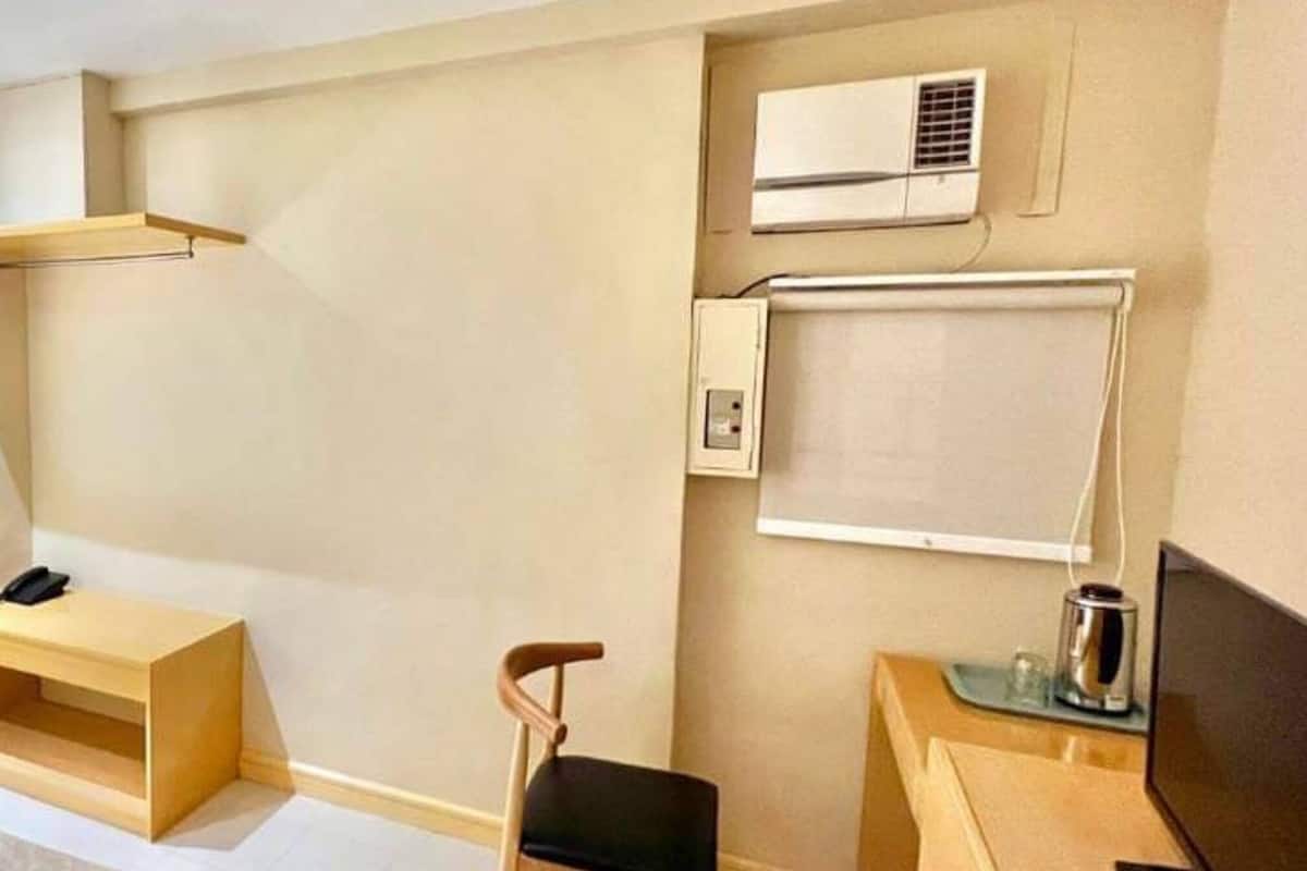 Ein Hotelzimmer mit Bett, Schreibtisch mit Computer, Stuhl, Klimaanlage und einem kleinen Schrank.