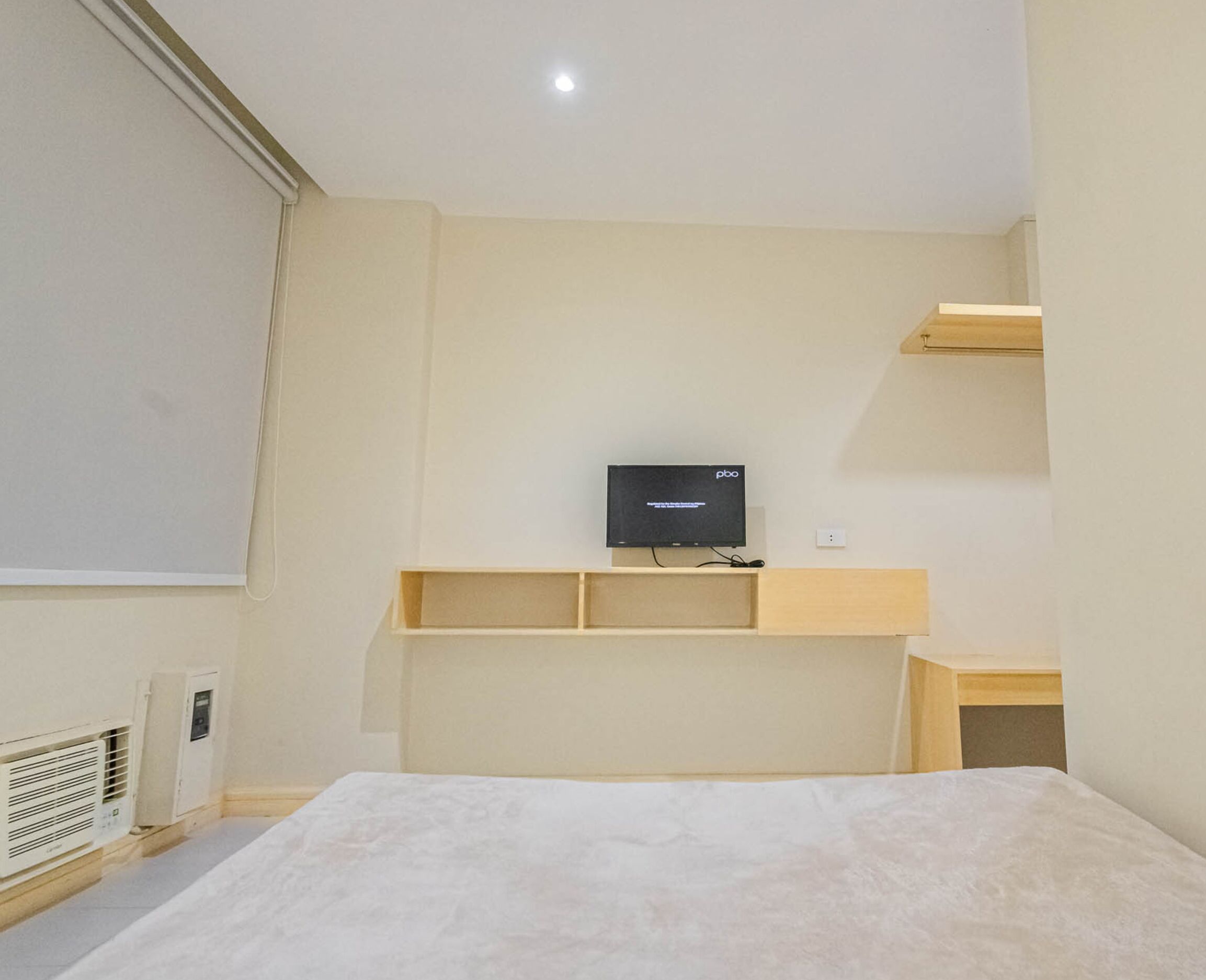 A bedroom with a bed, a television mounted on a wall, and a small wooden shelf.