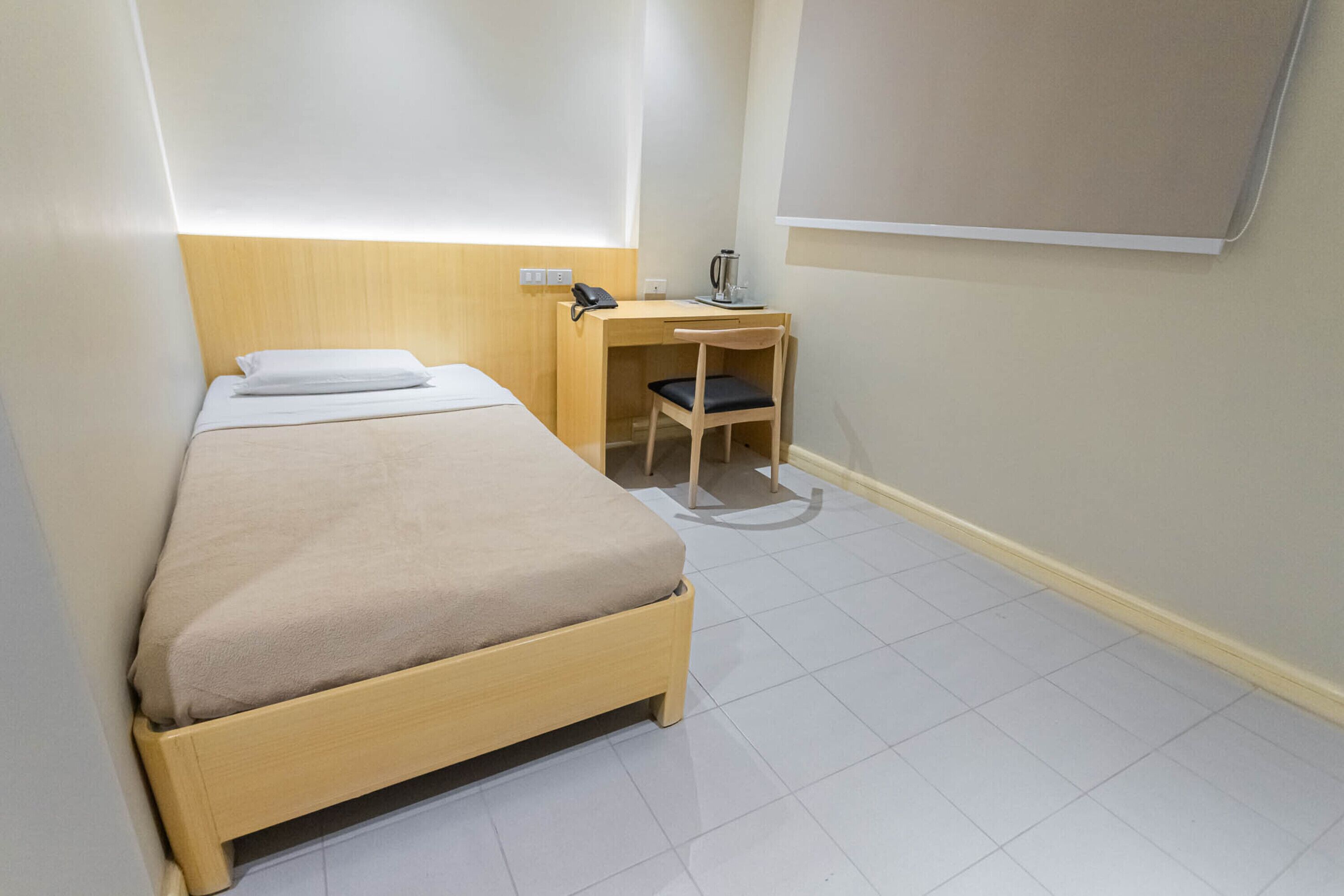 A small, neatly arranged room with a single bed, a desk with a chair, and a wall-mounted phone.