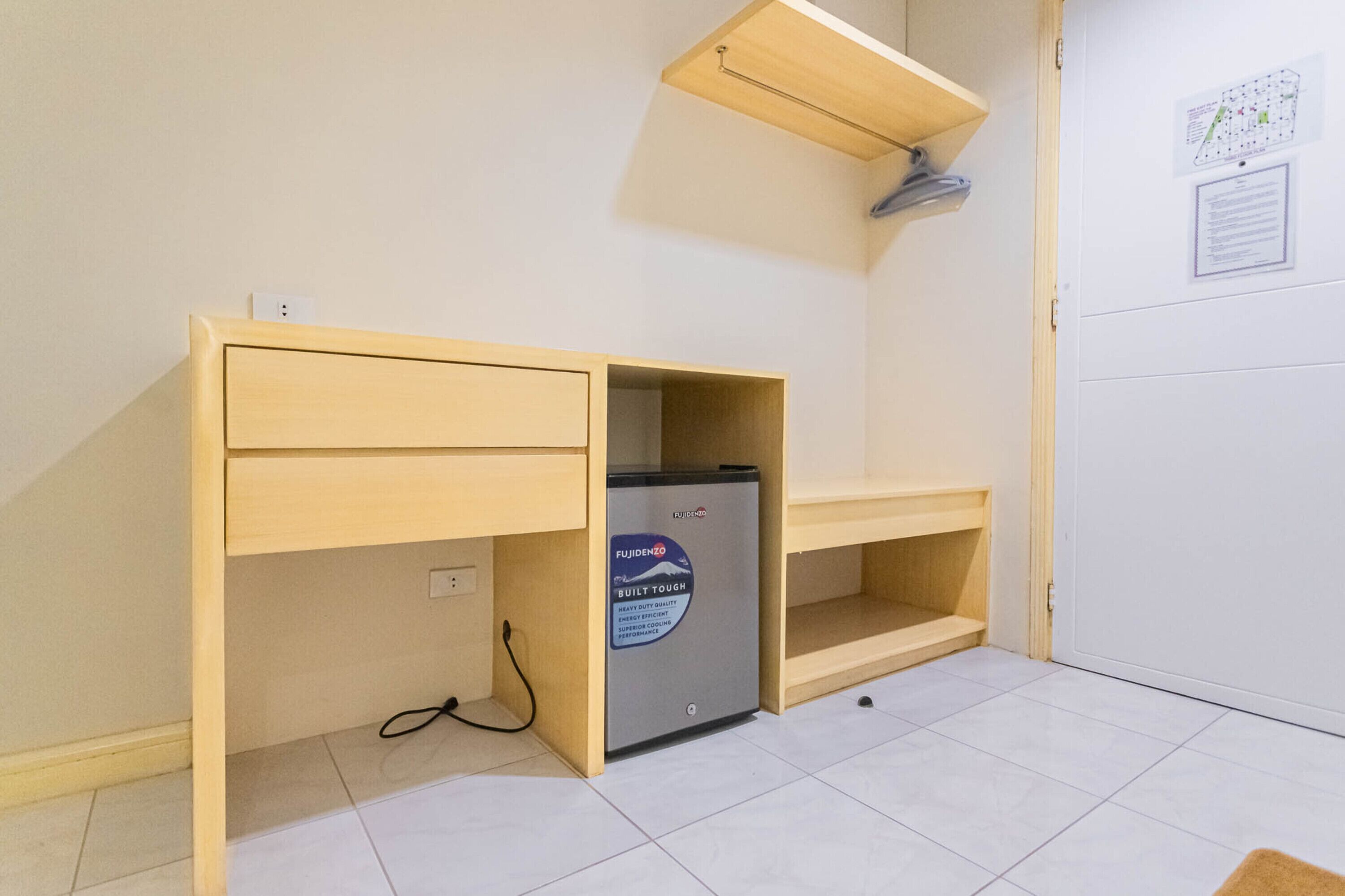 A compact room with a wooden desk, a small refrigerator, and a light shelf.