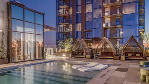 Ein modernes Hotel mit Poolbereich, großen Glasfenstern und Außenbestuhlung.