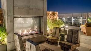 Ein moderner Außenbereich mit Sitzgelegenheiten, einem Kamin, Holzmöbeln und Blick auf die beleuchtete Stadt.