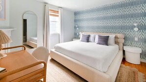 A bedroom with a large bed, a bedside table, a chair, and a window with curtains.