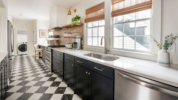 A modern kitchen with black and white checkered flooring, stainless steel appliances, and a large window with blinds. - The OakTree | DT Charleston Gem - Near King Street (Charleston)
