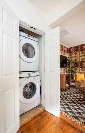 Laundry room with two front-loading washing machines and a wicker chair in the adjacent room.