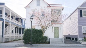 A white two-story house with a green door, a porch, and a tree with pink blossoms in front. - The OakTree | Bohemian Charm in DT Charleston! (Charleston)