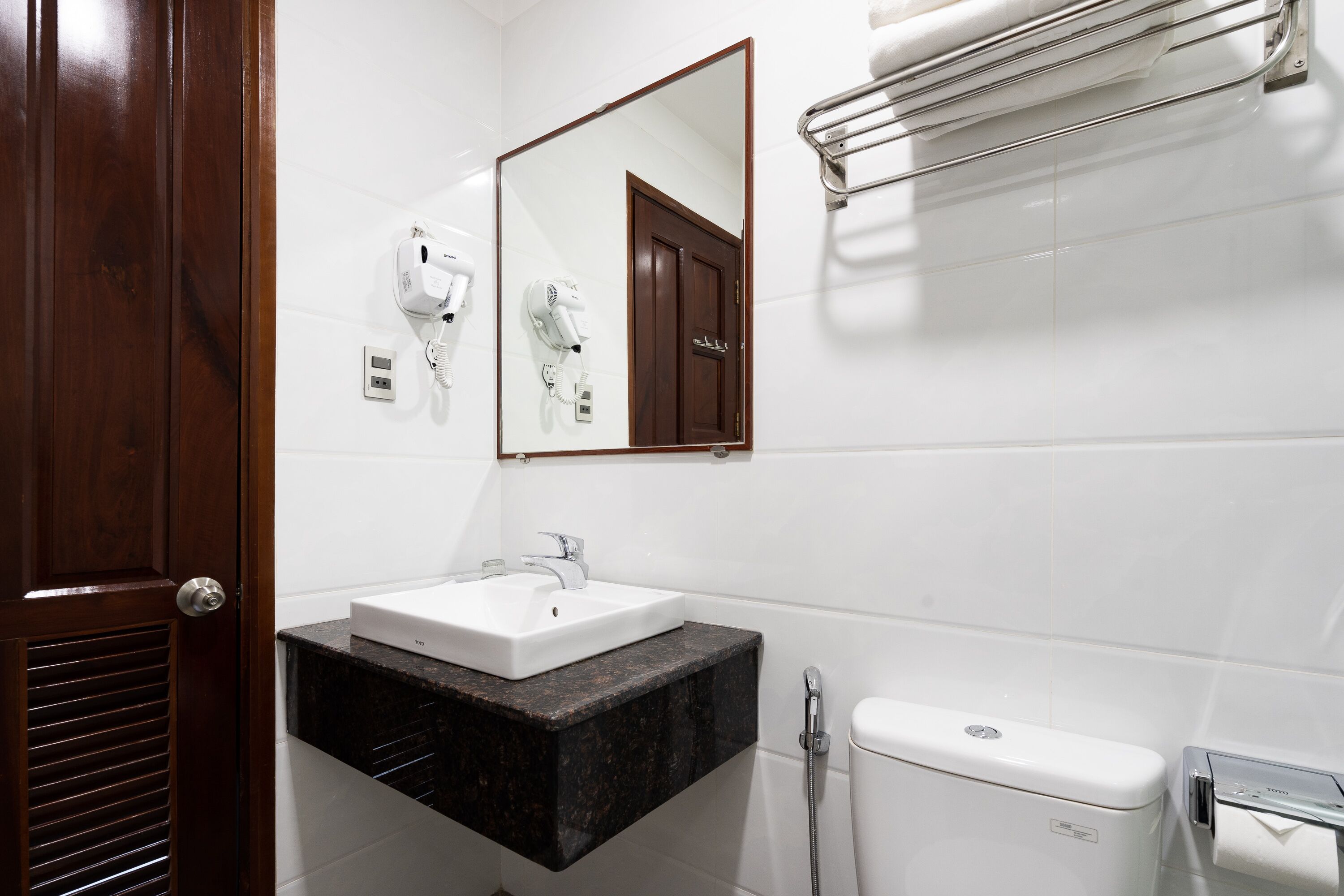 Une salle de bain avec un lavabo blanc, un miroir, un porte-serviettes et des toilettes.