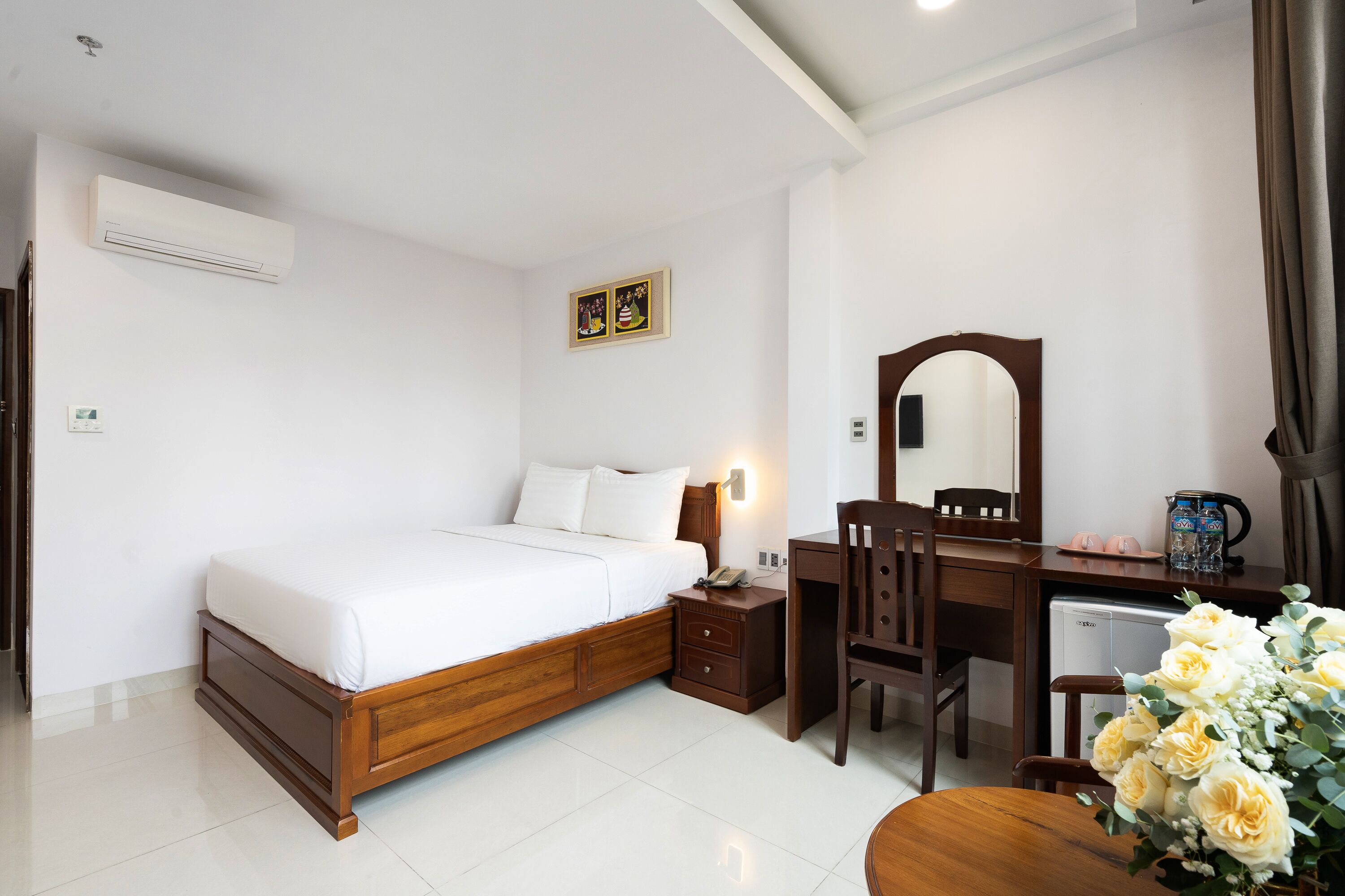 A bedroom with a bed, bedside table, desk, chair, and a mirror.