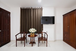A room with a wooden door, a TV mounted on the wall, a table with chairs, and a large cabinet.