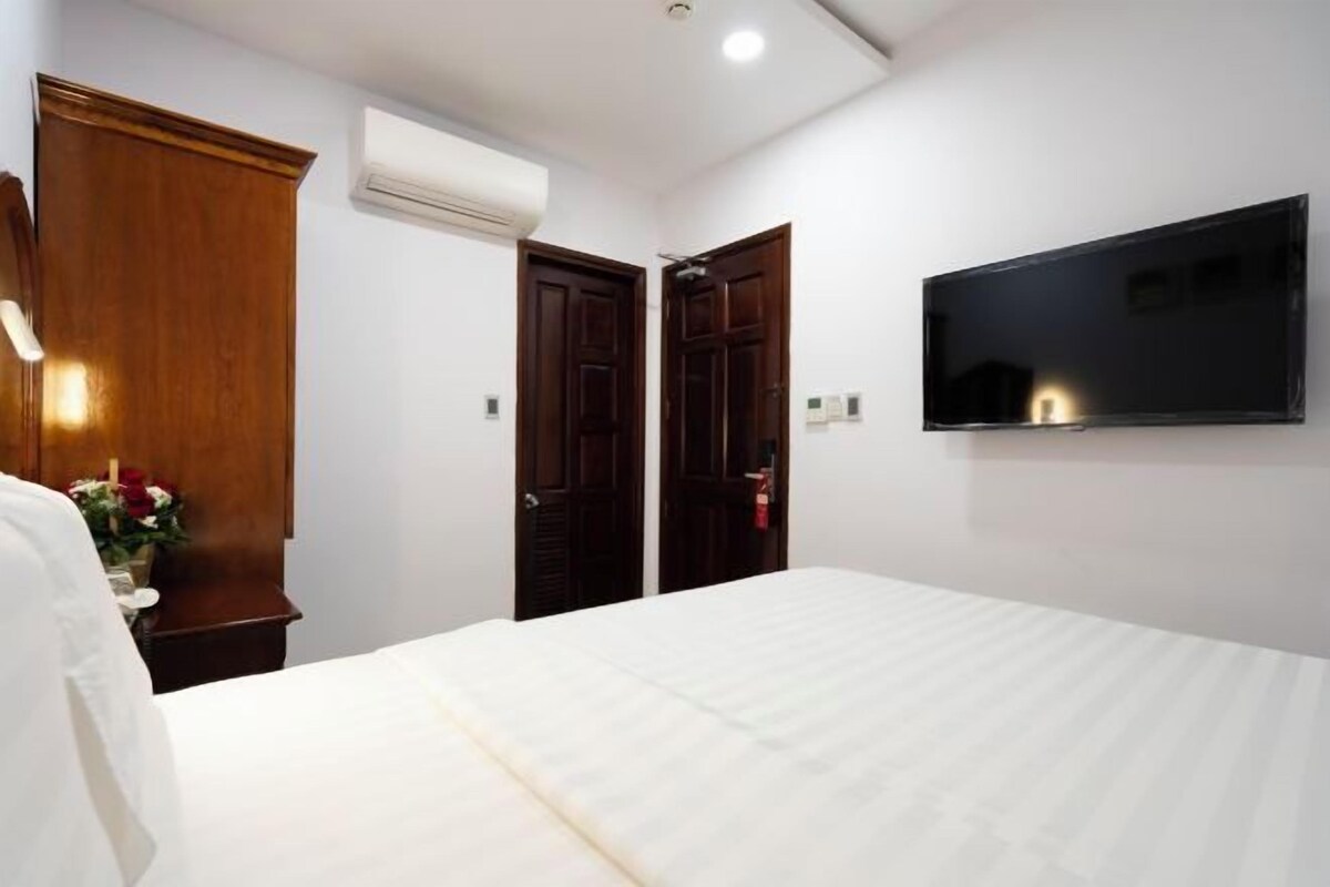 A hotel room with a bed, a TV mounted on the wall, and a wooden wardrobe.