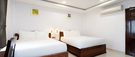 A hotel room with two wooden beds, white bedding, a ceiling light, an air conditioning unit, and a door.