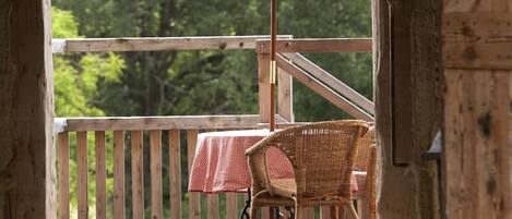 Eine Holzterrasse mit Tisch, Stühlen und einem Sonnenschirm, mit Blick auf Bäume.