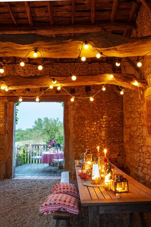 A rustic dining area with a stone wall, wooden beams, and string lights. - Studio apartment over looking the beautiful French countryside. (Beauville)
