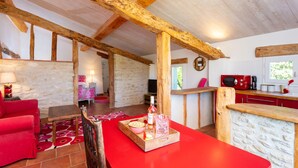 Quarto espaçoso com vigas de madeira aparentes, uma mesa vermelha com uma bandeja de petiscos, parede de pedra e vista para o exterior.