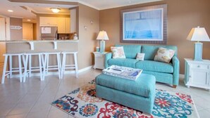 Ein Wohnzimmer mit einem türkisfarbenen Sofa, einem Couchtisch, einem gemusterten Teppich und einem Deckenventilator.