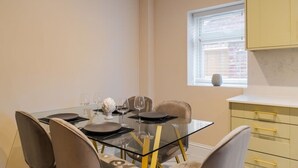 A dining area with a glass table, chairs, and a window with blinds. - 2BR Gem, Parking & Garden - VAT Q - By Tempstay (Berkshire)