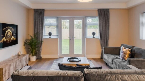 A living room with a sofa, a coffee table, a TV mounted on the wall, and a large window with curtains. - 2BR Gem, Parking & Garden - VAT Q - By Tempstay (Berkshire)