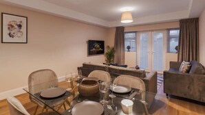 A dining area with a glass table, chairs, and a sofa in the background. - 3BR Home, Parking, Garden - VAT Q - By Tempstay (Windsor)