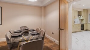A dining area with a glass table, leather chairs, and a wooden door leading to a kitchen. - 3BR Home, Parking, Garden - VAT Q - By Tempstay (Windsor)