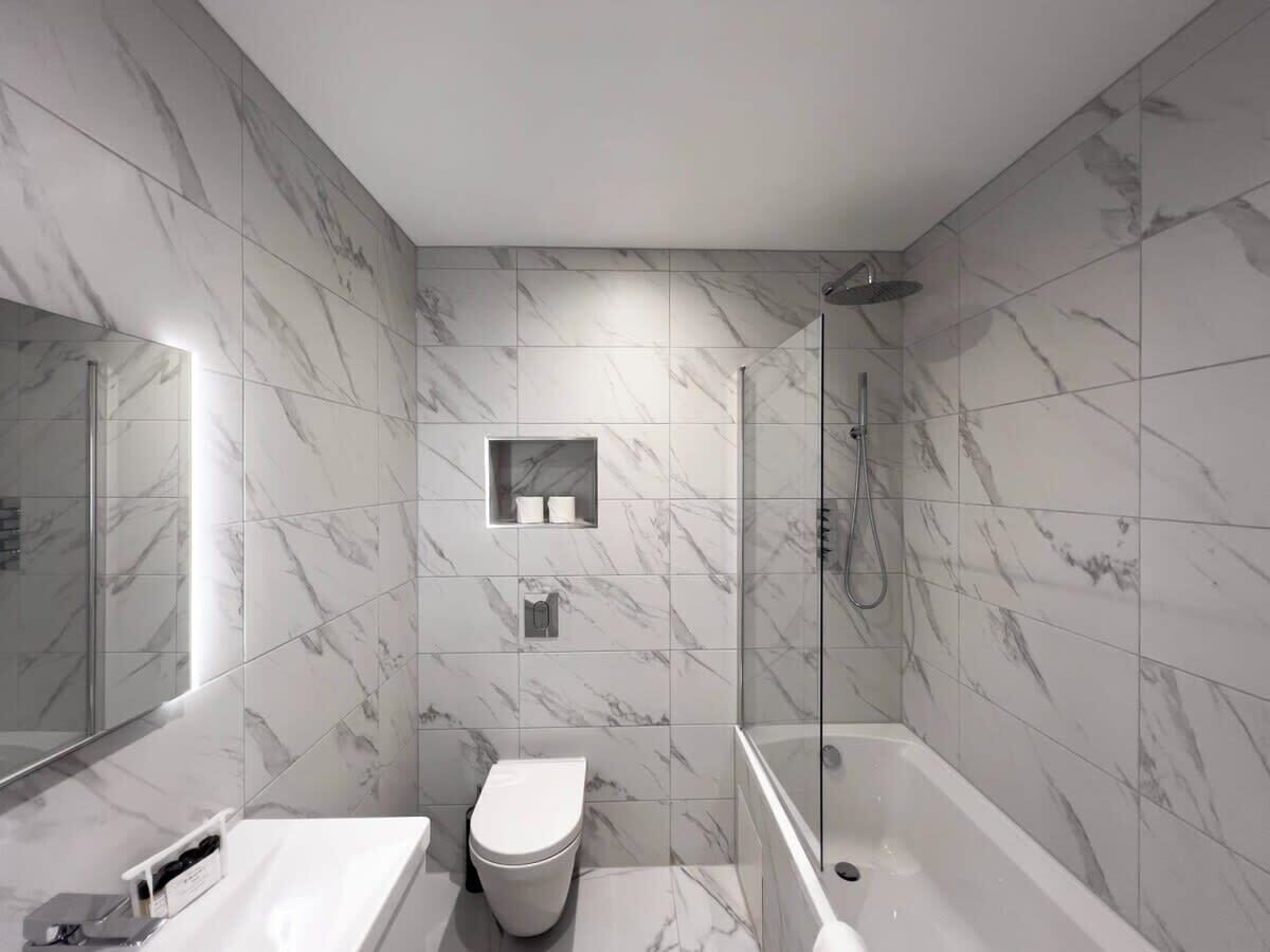 Et moderne badeværelse med brusekabine i glas, toilet i hvidt og badekar.