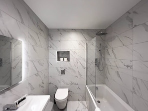 Une salle de bain moderne avec une douche à parois de verre, des toilettes blanches et une baignoire.