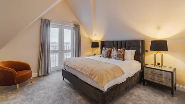 Une chambre à coucher avec un grand lit, deux tables de chevet, une chaise et une fenêtre avec des rideaux.