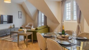 Un coin repas avec une table dressée pour deux personnes, un canapé et un téléviseur en arrière-plan.