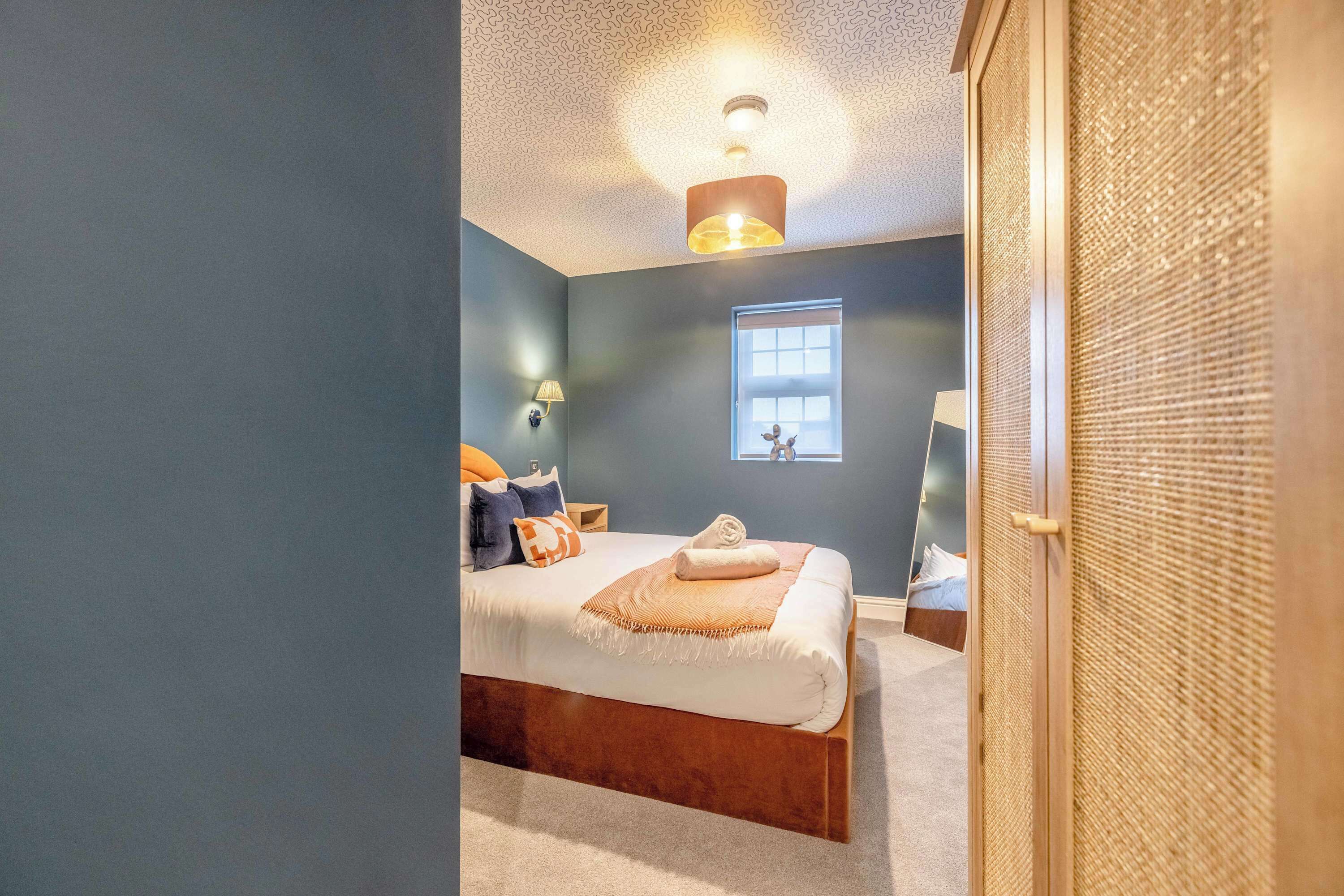 A bedroom with a bed, a window, a lamp, and a ceiling light.