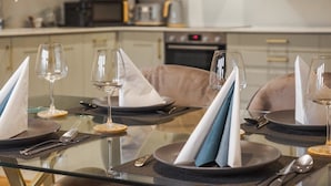 A dining table set with plates, cutlery, and wine glasses, with a modern kitchen in the background. - Castle Views| 2 Bed |Parking - VAT Q - By Tempstay (Berkshire)
