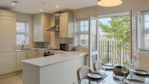 A modern kitchen with a central island, a dining area with a glass table, and a balcony with a view. - Chic 2 Bed Flat - Balcony - Parking - By Tempstay (Berkshire)
