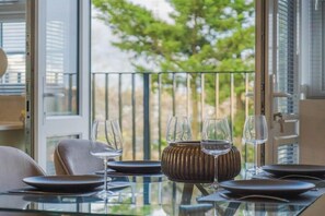 A dining table set with plates, glasses, and a decorative vase, with a view of greenery through a balcony door. - Chic 2 Bed Flat - Balcony - Parking - By Tempstay (Berkshire)
