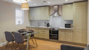 A modern kitchen with light-colored cabinets, a stainless steel range hood, and a dining area with a glass table and chairs. - 1BR Gem, Private Parking - VAT Q - By Tempstay (Berkshire)