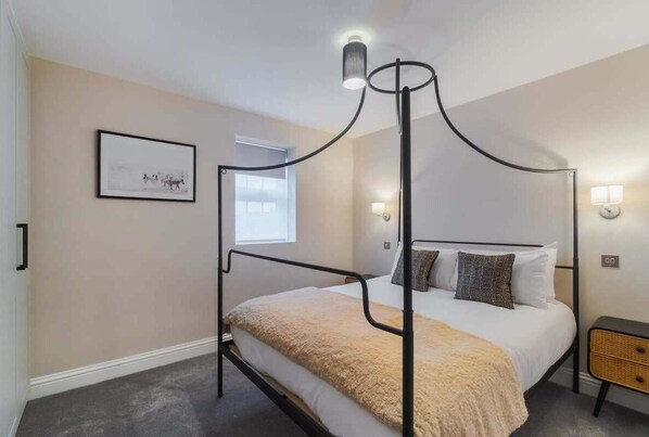 Un lit à baldaquin avec une couverture beige, un tableau encadré au mur et une lampe de chevet.
