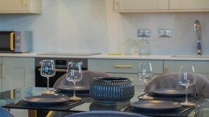 A dining area with a glass table, dark plates, and wine glasses. - Charming 2 BDR in Windsor - VAT Q - By Tempstay (Berkshire)