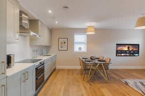 Una cocina moderna con electrodomésticos integrados, un comedor con mesa de vidrio y un televisor montado en la pared.