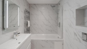 A modern bathroom with a white marble wall, a large mirror, a bathtub, and a shower enclosure. - Charming 2 BDR in Windsor - VAT Q - By Tempstay (Berkshire)