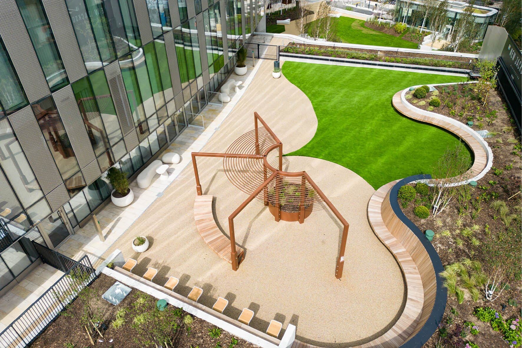 Un bâtiment moderne doté d’une façade en verre, d’une sculpture centrale et d’un jardin aménagé.