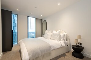 Un dormitorio moderno con una cama grande, una mesita de noche y vistas de la ciudad a través de las ventanas.