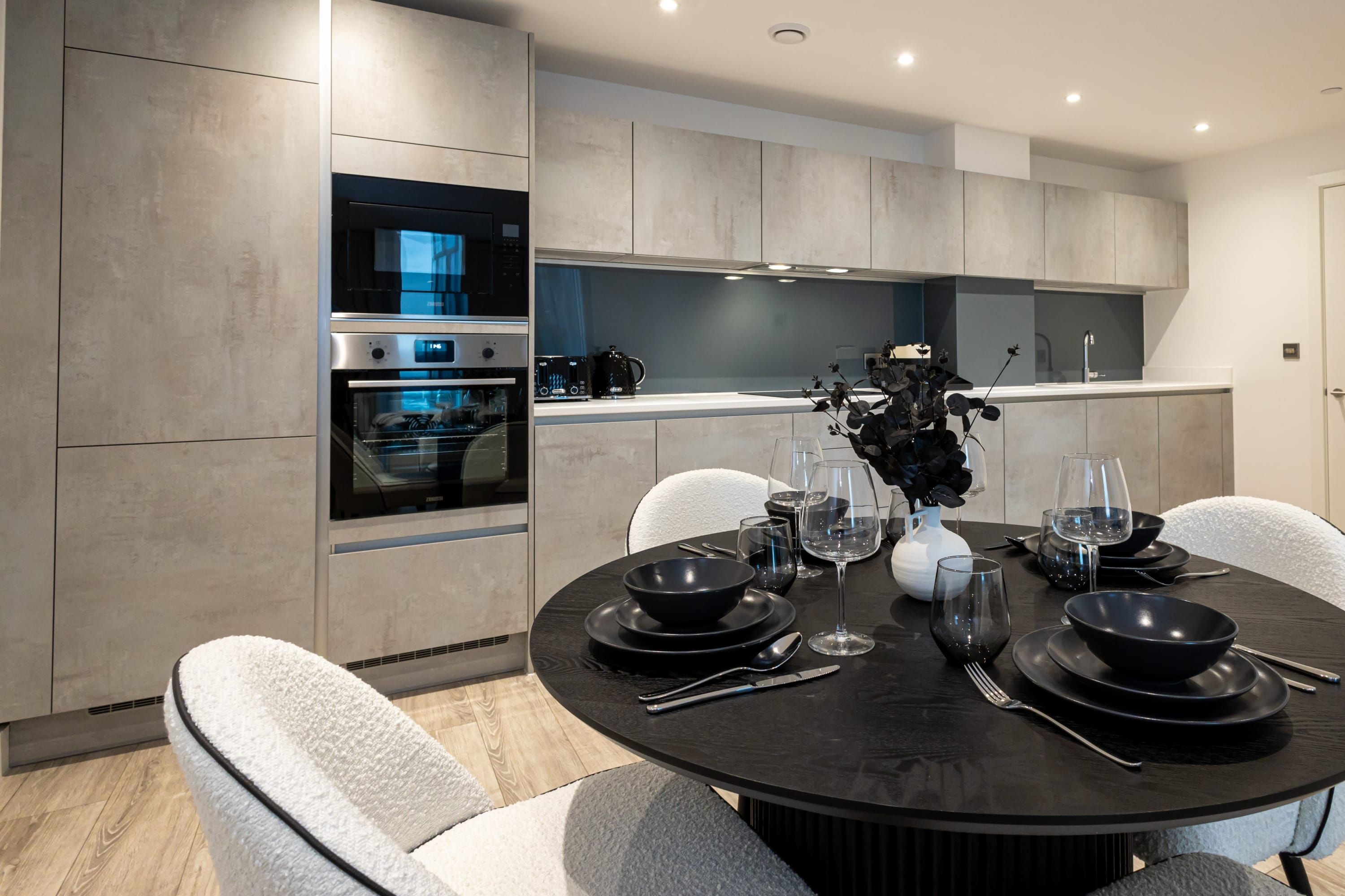 Een moderne keuken met inbouwapparatuur, een eethoek met een ronde tafel voor zes personen, en een uitzicht op de aangrenzende eetkamer.